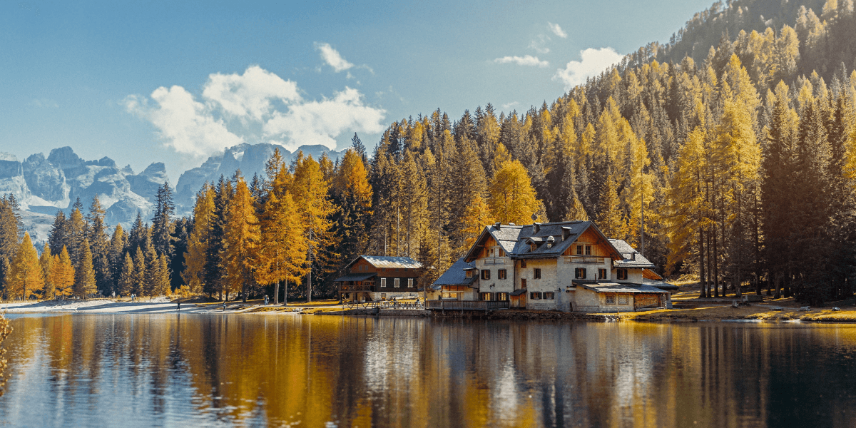 Alpenmeer dat een herfstbos en een chalet weerspiegelt, met ruige bergen op de achtergrond