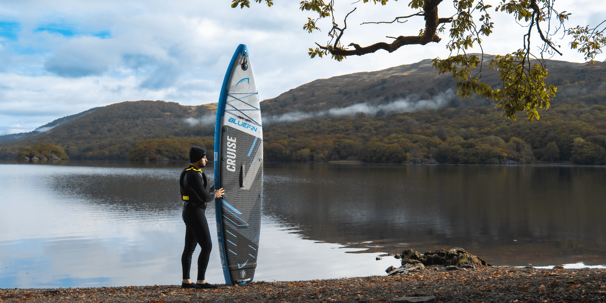 Man holding blue original paddleboard on the edge of a autumnal lake