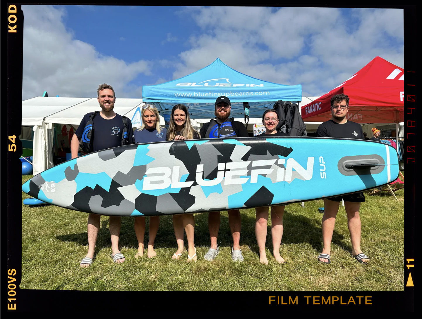 Group of five people holding a Bluefin SUP paddleboard with a blue and gray camo design outdoors
