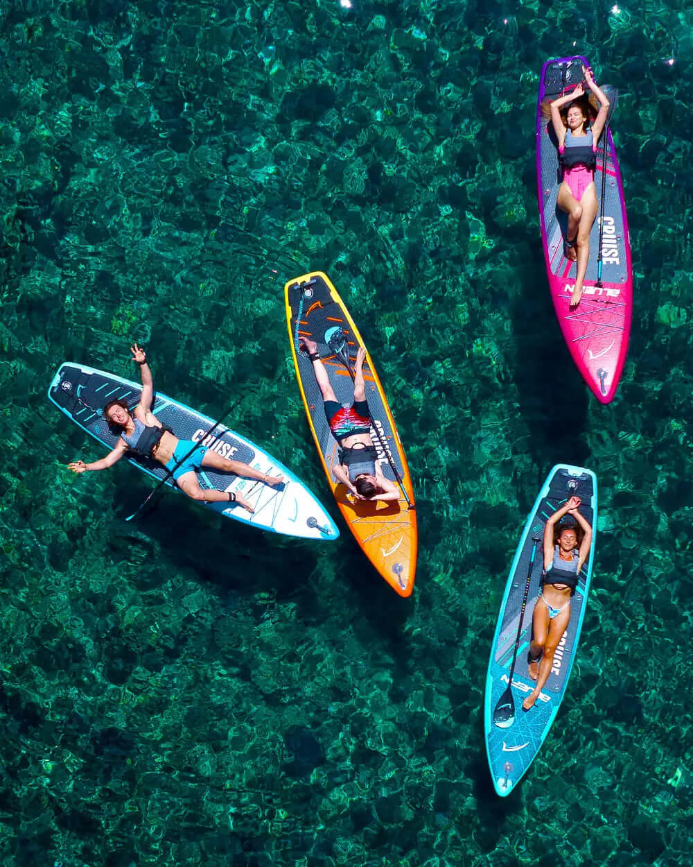 Four paddleboarders relaxing on colorful boards in clear water, enjoying a sunny day.