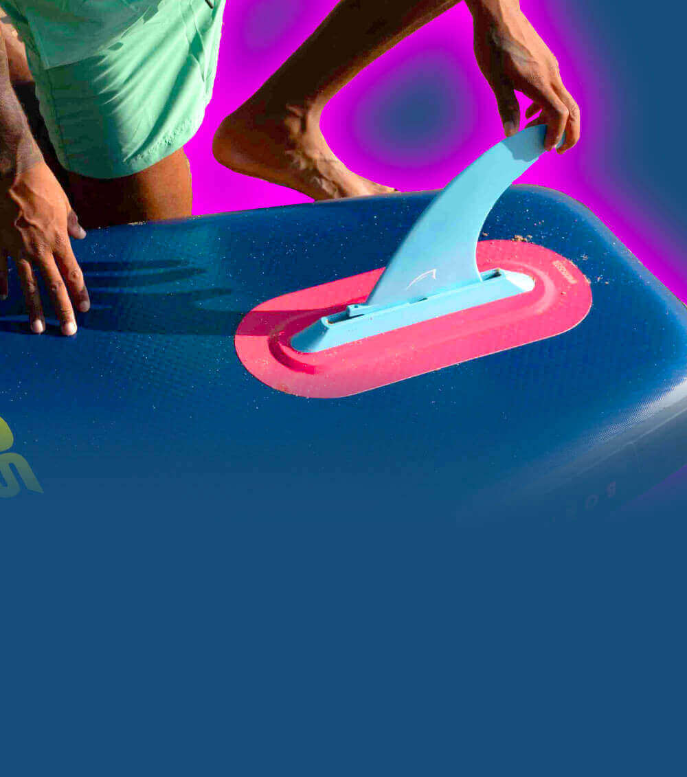 Person attaching a blue fin to a paddleboard with a textured surface and red base