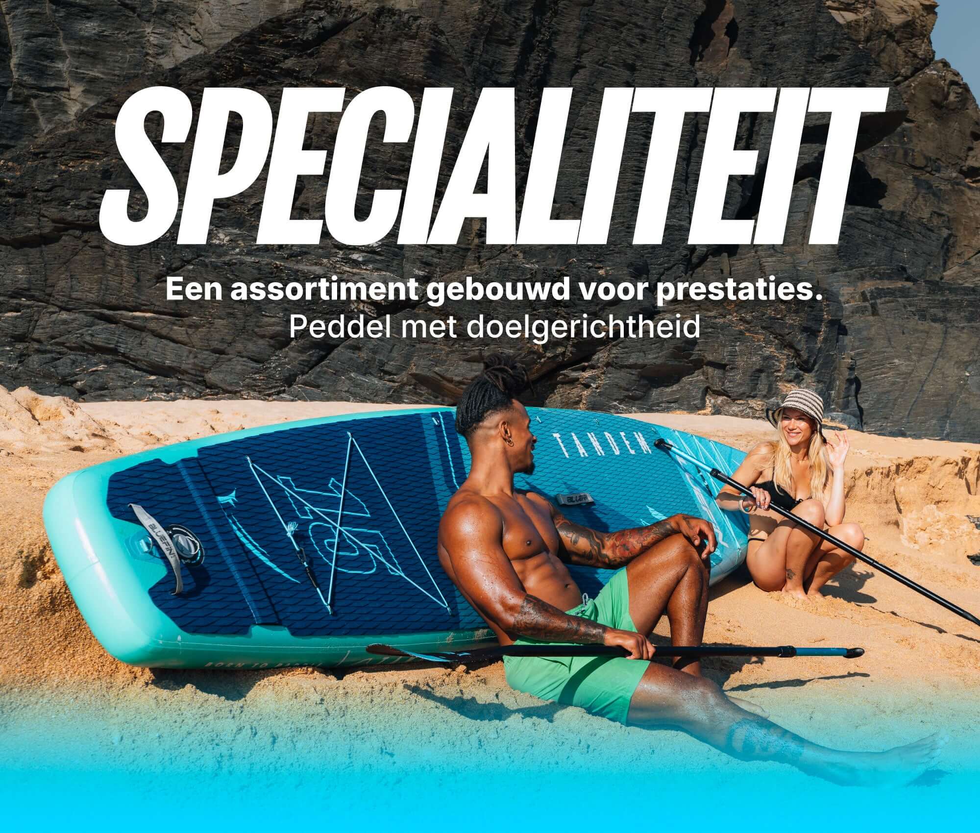 Two people on a beach with a blue inflatable paddleboard, one sitting and one kneeling with paddles.