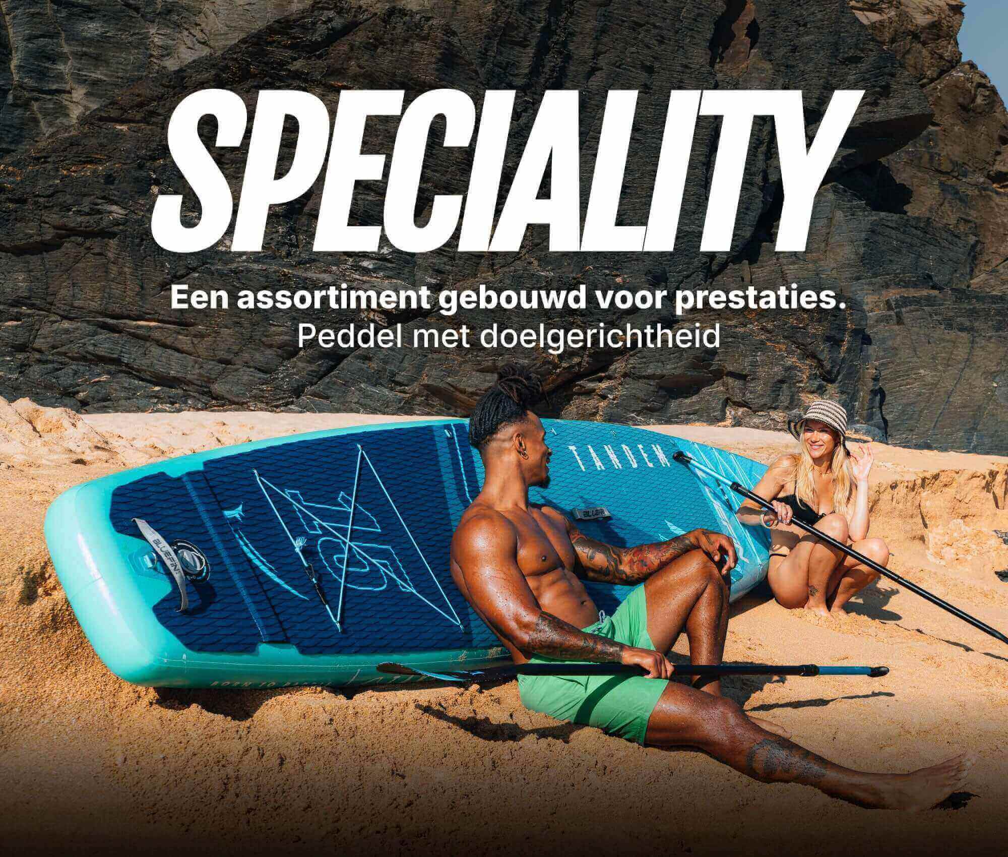 Two people on a beach with a blue inflatable paddleboard, one sitting and one holding a paddle.