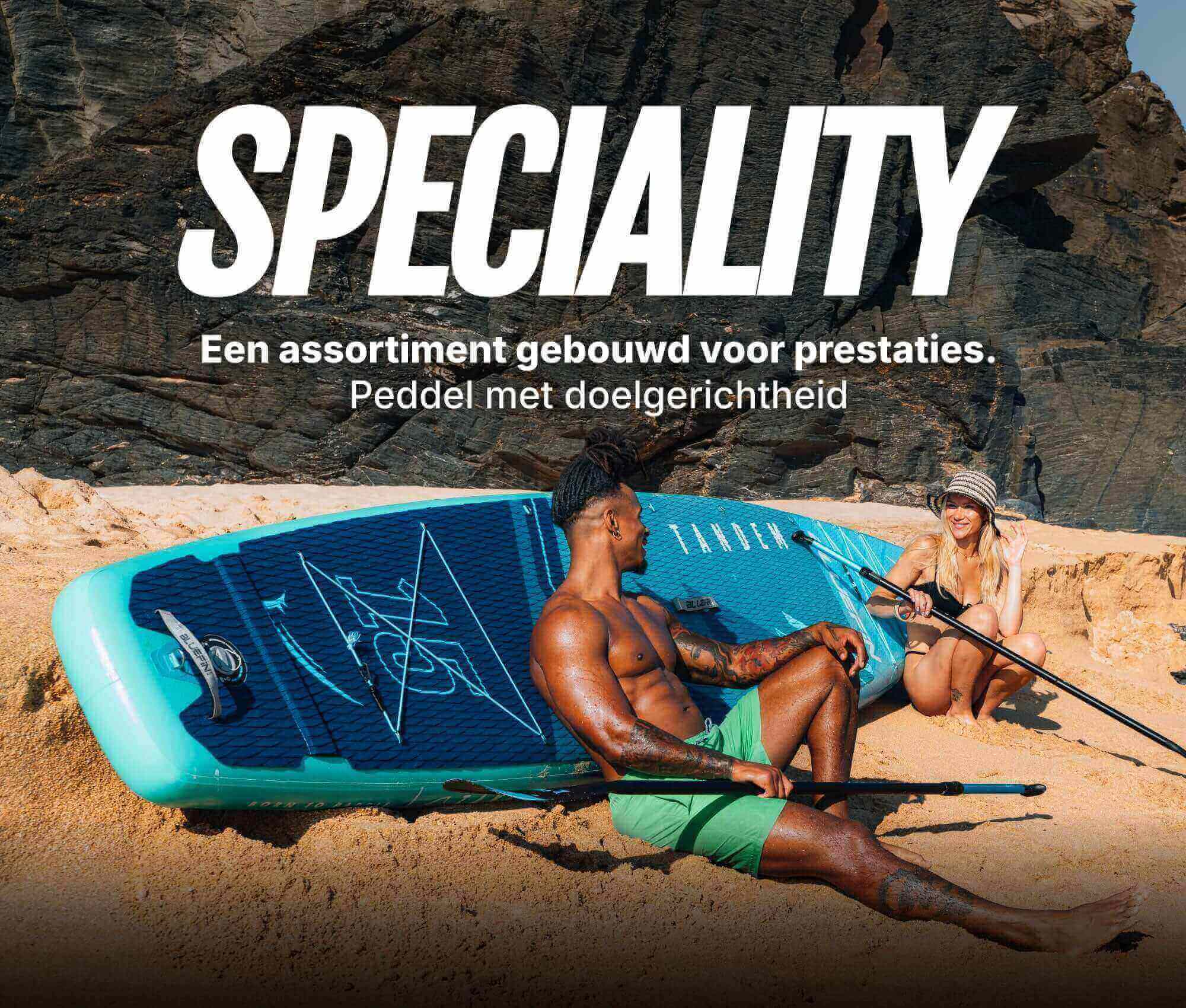 Two people on a beach with a blue inflatable paddleboard, one sitting and one holding a paddle.