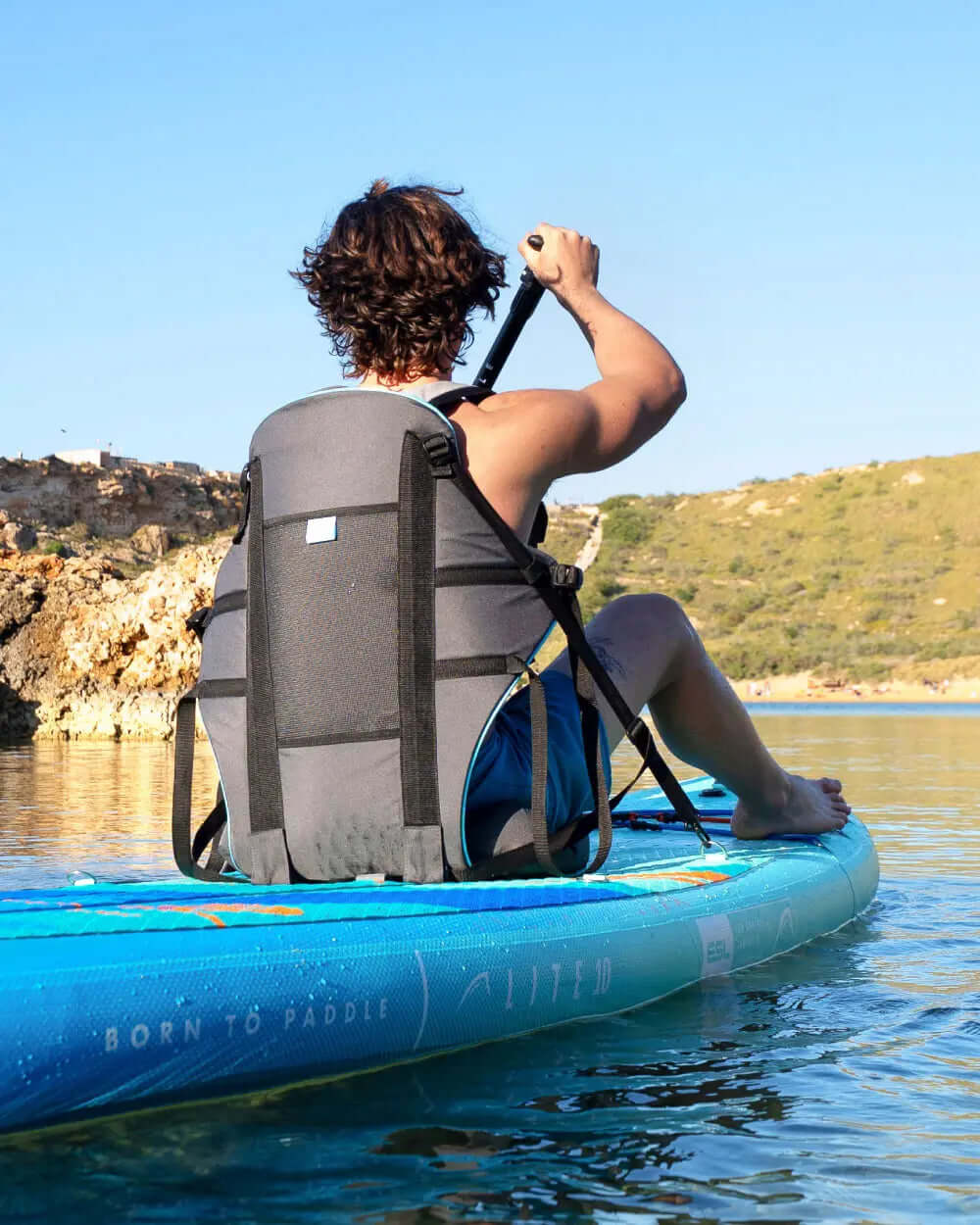 Person paddling on a blue inflatable paddleboard with a gray backrest in calm water