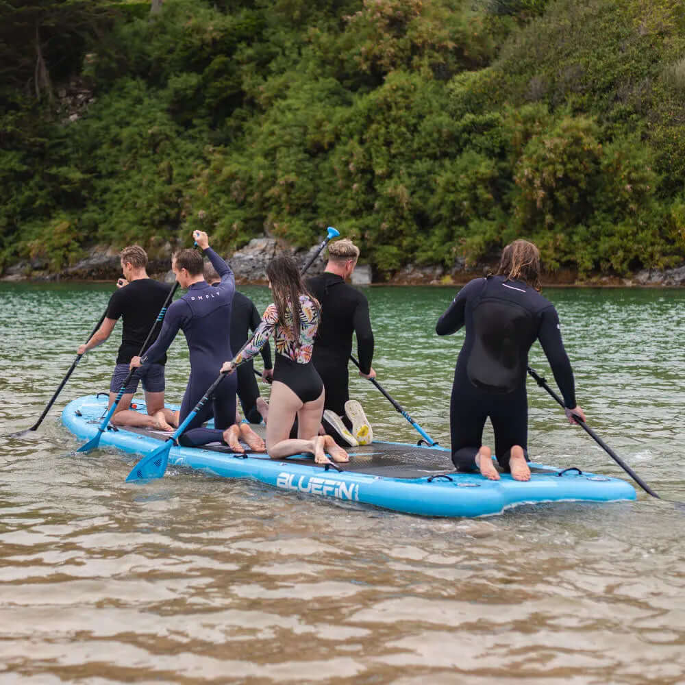 Groep van zes mensen die peddelen op een blauw opblaasbaar paddleboard in kalm water