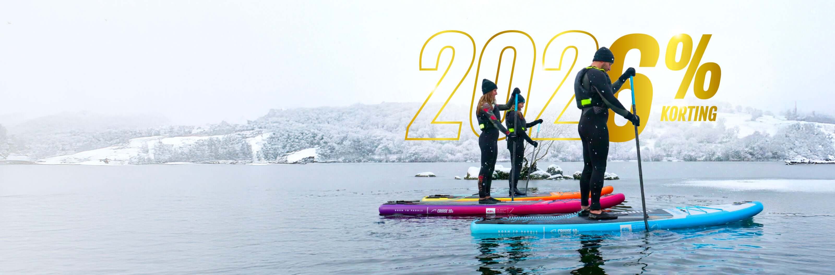Three paddleboarders on colorful boards in winter scenery, snow-covered hills in background.