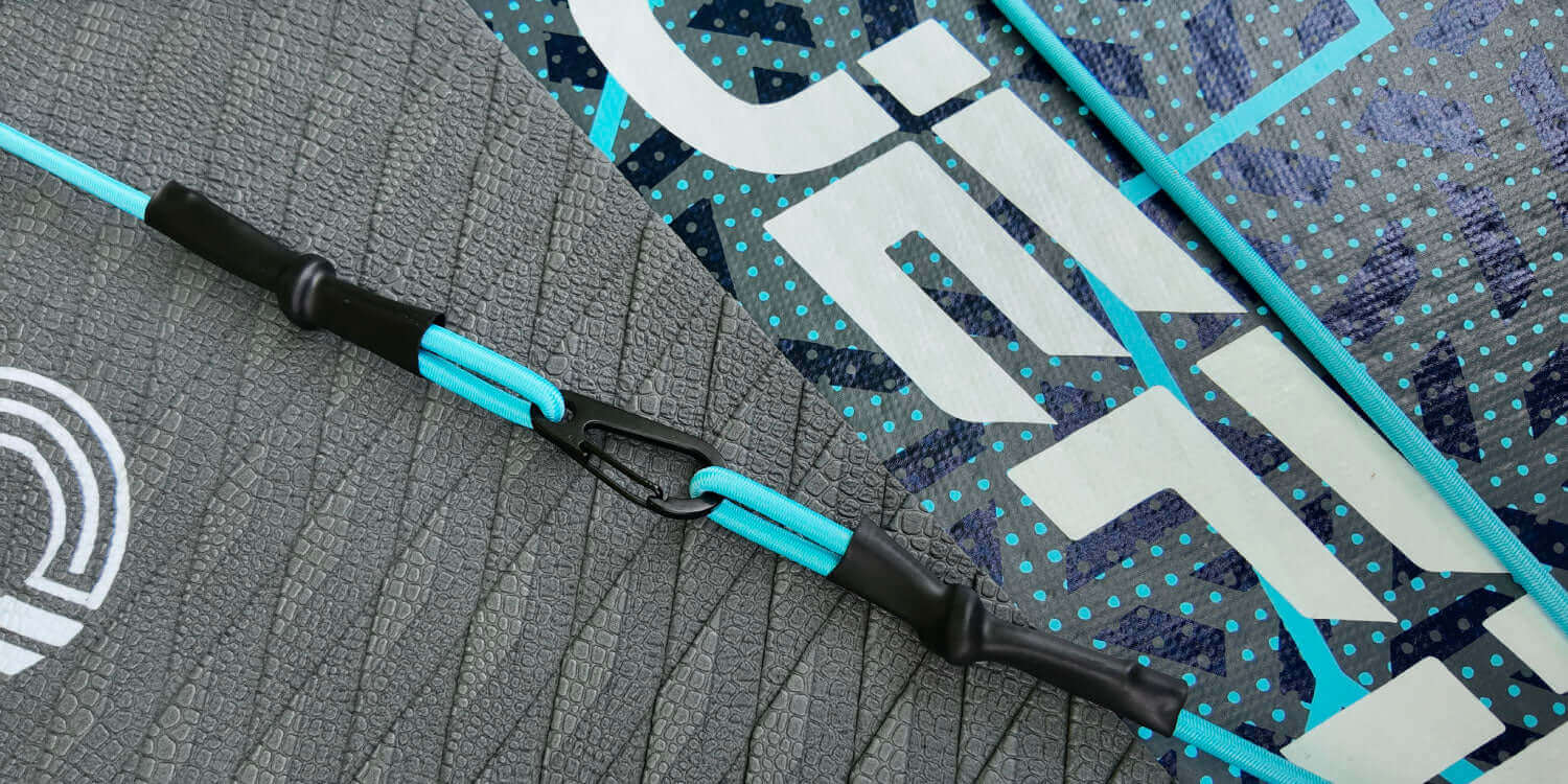 Close-up of a paddleboard's textured surface, featuring a blue safety leash and attachment clip.