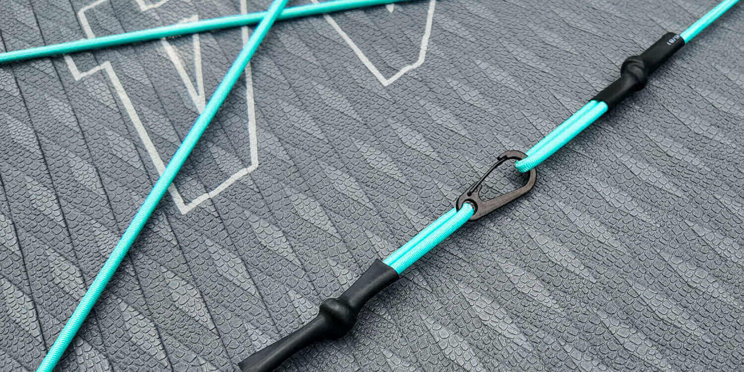 Close-up of a turquoise paddleboard leash with a black clip on a textured gray surface