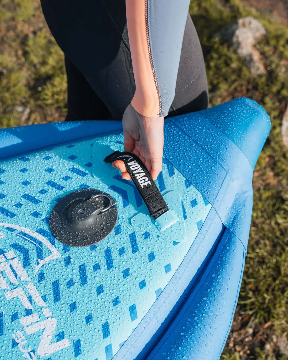 Person holding a blue inflatable paddleboard with a textured deck and water droplets on it