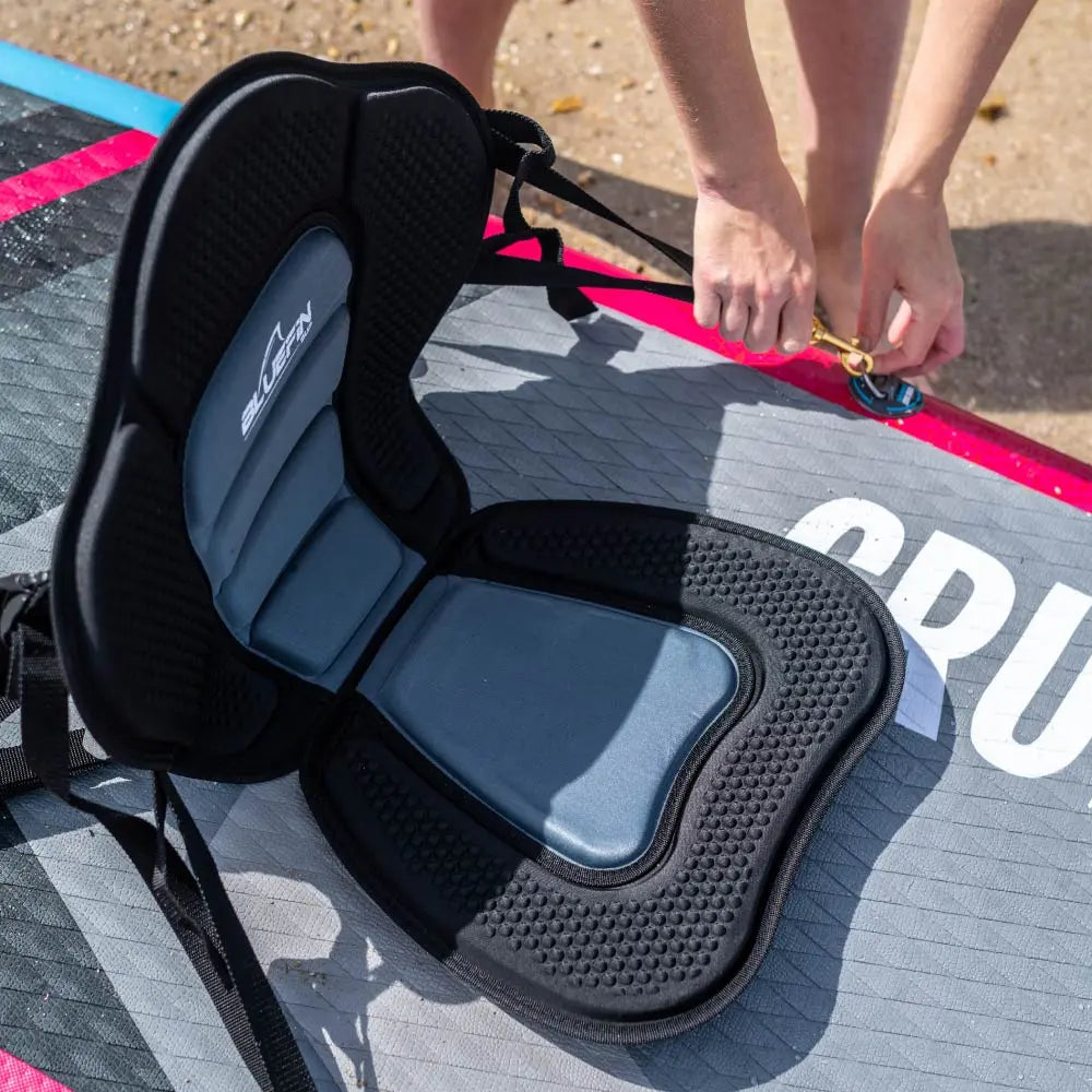 Black and gray padded seat on a paddleboard, with a person attaching a strap.