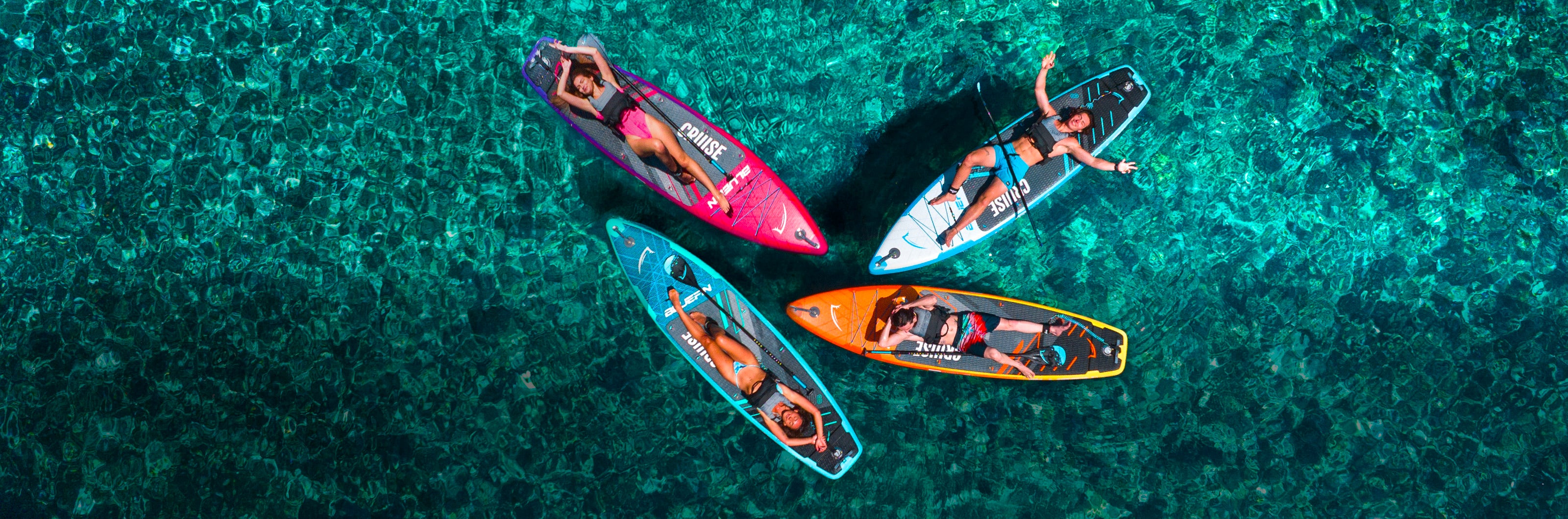 Four paddleboarders on colorful boards in clear turquoise water, enjoying a sunny day outdoors.