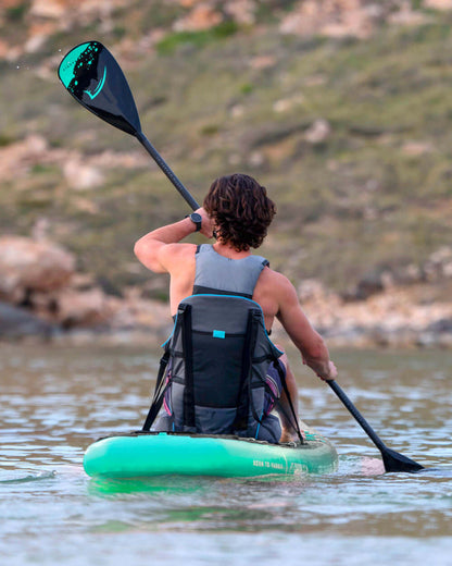 Person paddling a green inflatable paddleboard with a black paddle in calm water