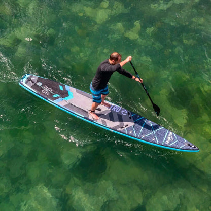 Man die peddelt op een blauw en zwart opblaasbaar paddleboard over helder groen water