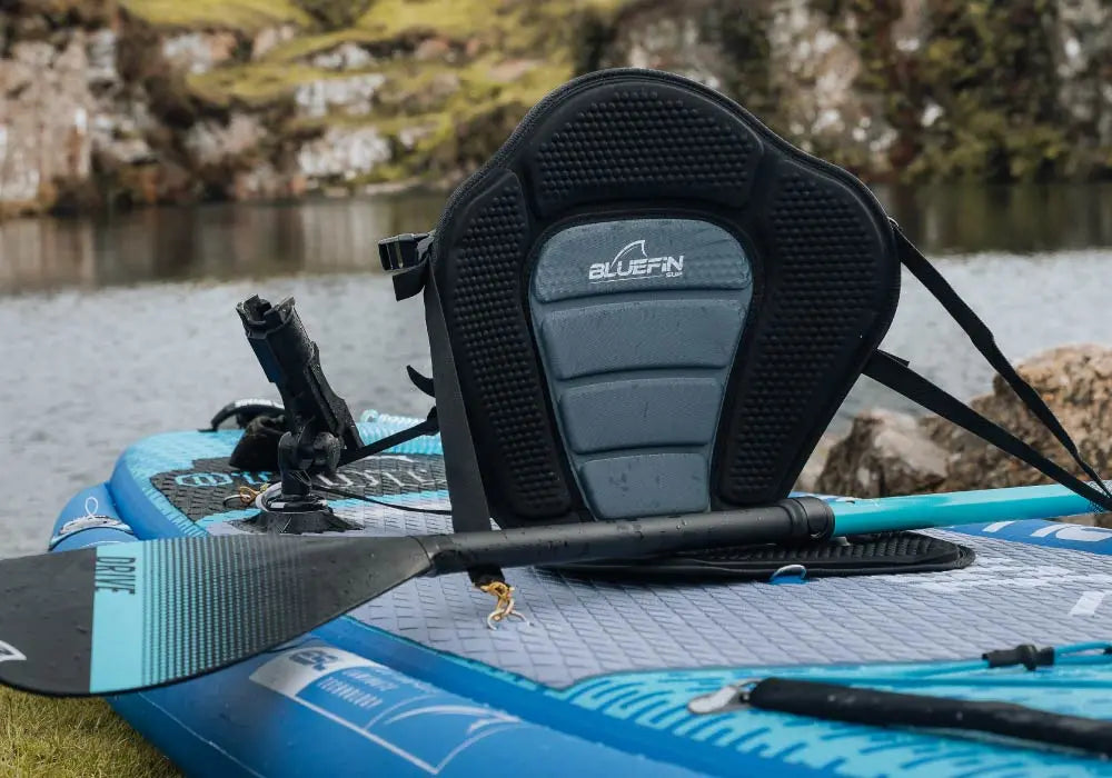 Inflatable paddleboard with a Bluefin seat, paddle, and a scenic lake background.